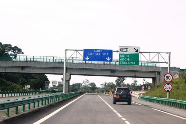 A newly constructed asphalt road with streetlights and pedestrian walkways in Cameroon, surrounded by green vegetation and blue sky.